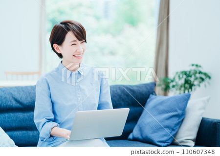 A middle-aged woman who operates a laptop in the living room. A middle-aged woman who operates a laptop in the living room. 110607348