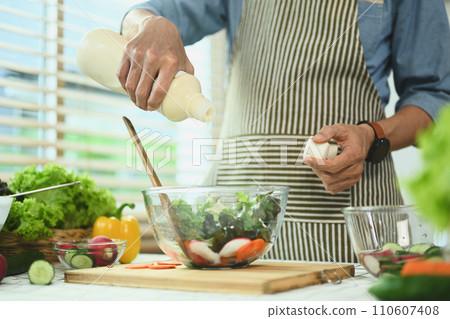 Senior man pouring dressing into bowl with fresh vegetable salad. Healthy eating and culinary concept 110607408