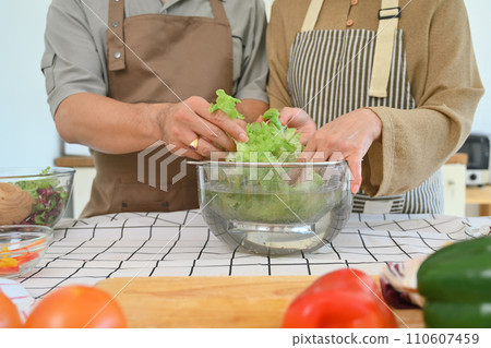 Hands of senior couple sorting out fresh vegetables preparing a fresh healthy vegan salad in kitchen 110607459