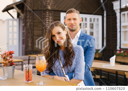 Portrait of a stylish young couple in love in blue flowers in summer in the city at a bar table, drinking cocktails Portrait of a stylish young couple in love in blue flowers in summer in the city at a bar table, drinking cocktails 110607820