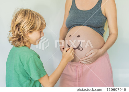 Adorable moment as a son adds a touch of joy to his mother's pregnancy, playfully drawing a funny face on her baby bump, creating cherished memories 110607946