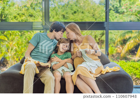 Heartwarming family moment as expectant mom, dad, and son joyfully browse through newborn baby's clothes, eagerly anticipating the arrival of a new family member 110607948