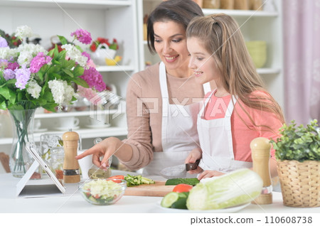 Smiling mother and daughter cooking together at kitchen 110608738