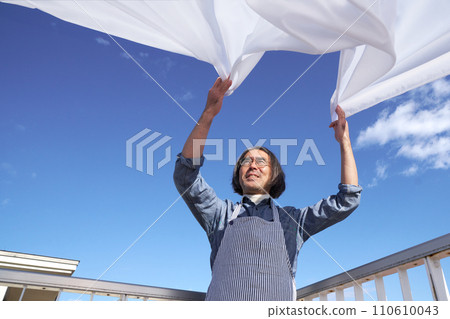 一位中年家庭主婦在藍天下舖開洗衣床單。 一位中年家庭主婦在藍天下舖開洗衣床單。 110610043