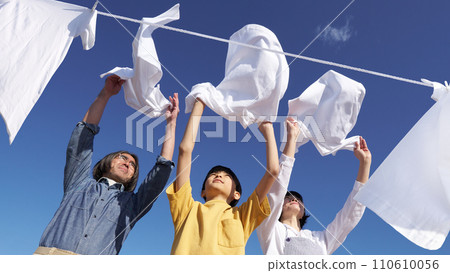 A family of three hanging out their laundry to dry under the blue sky A family of three hanging out their laundry to dry under the blue sky 110610056