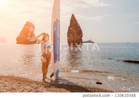 Woman sea sup. Close up portrait of happy young caucasian woman with long hair looking at camera and smiling. Cute woman portrait in bikini posing on sup board in the sea 110610388
