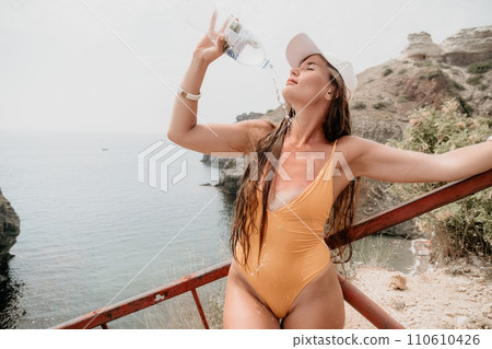 Woman travel sea. Happy tourist enjoy taking picture outdoors for memories. Woman traveler drinks water at the edge of the cliff on the sea bay of mountains, sharing travel adventure journey Woman travel sea. Happy tourist enjoy taking picture outdoors for memories. Woman traveler drinks water at the edge of the cliff on the sea bay of mountains, sharing travel adventure journey 110610426