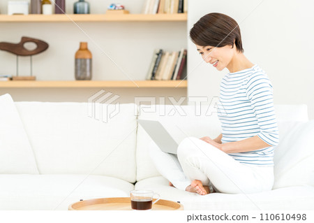 A middle-aged woman operates a laptop in the living room. 110610498