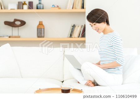 一位中年婦女在客廳操作筆記型電腦。 110610499