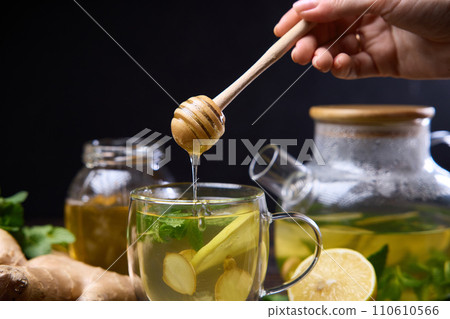 woman pours honey in a cup with natural organic herbal tea and glass teapot on a wooden table woman pours honey in a cup with natural organic herbal tea and glass teapot on a wooden table 110610566