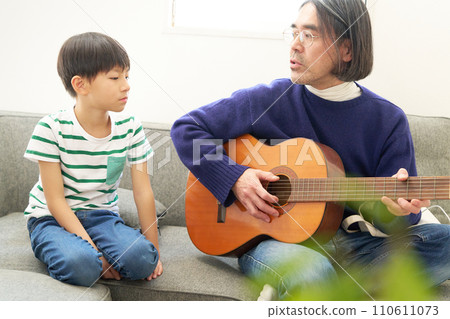 A father playing the guitar and his young son looking at him 110611073
