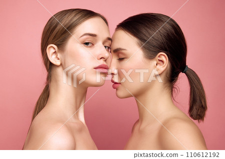 Unfiltered charm. Girls embrace natural beauty as one. Close up of two pretty ladies with bare shoulders posing against pink studio background. 110612192