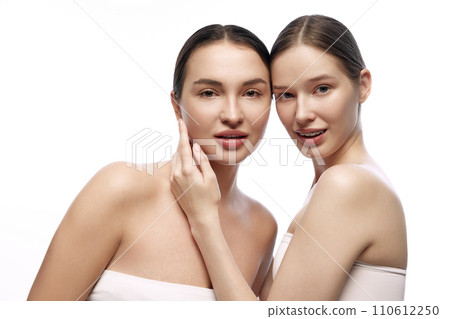 Portrait of two positive two beautiful, young Caucasian women with light standing unembraced against white studio background. Portrait of two positive two beautiful, young Caucasian women with light standing unembraced against white studio background. 110612250