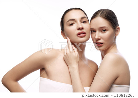 Cheerful young women with smooth, fresh skin posing while standing together against white studio background. 110612263