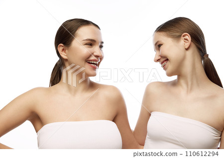 Two women with natural makeup, highlighting their clear skin and subtle beauty features against white studio background. 110612294
