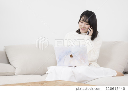 女人一邊打電話一邊看著沙發上的筆記型電腦 女人一邊打電話一邊看著沙發上的筆記型電腦 110612440