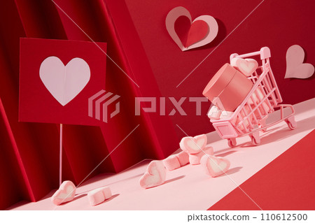A composition with two tones of pink and red with a mini trolley containing marshmallows and a cream jar without label. Lots of heart-shaped marshmallows and heart papers decorated 110612500
