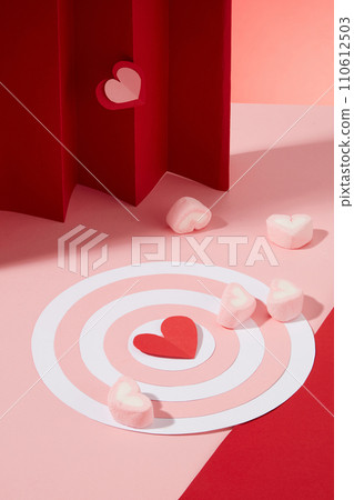 Women day and Valentine day concept with a bullseye in pink and white color decorated with several heart-shaped marshmallows. Red paper heart origami featured. Template for design 110612503