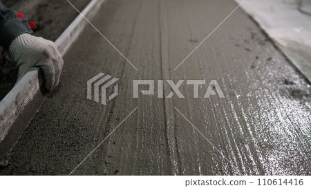 A builder uses a trowel to level a cement mortar screed. Concrete work on a construction site. Installation work using trowels. Leveling fresh mortar using a tool. 110614416