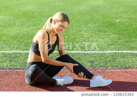 Fitness enthusiast feeling discomfort in her leg on the track field, indicating a potential injury or strain. 110615363