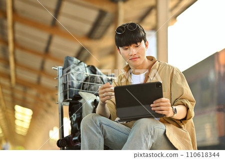 Young man using digital tablet, checking the route of trip on map while waiting train. 110618344