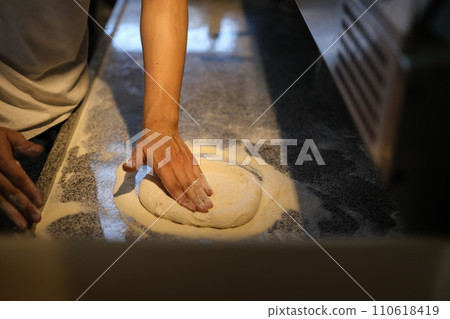 Chef kneading pizza dough with flour on kitchen table. Bakery or pizza baking concept 110618419