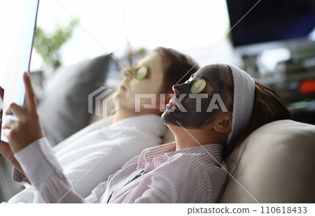 Young man and woman lying on couch with moisturizing face masks 110618433