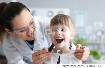 Dentist examining mouth of little girl with instruments 110618435