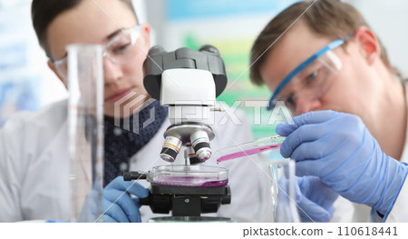 Man and woman pouring liquid from test tube into petri dish closeup Man and woman pouring liquid from test tube into petri dish closeup 110618441