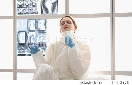 Tired doctor in protective suit sits on floor with X-rays hanging in background Tired doctor in protective suit sits on floor with X-rays hanging in background 110618578
