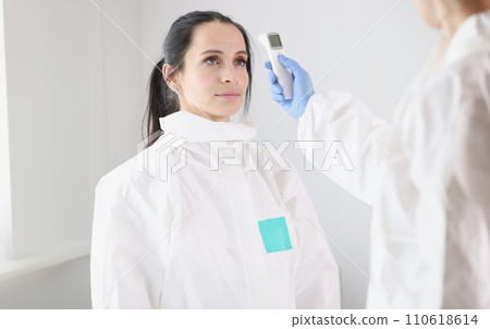 For doctor in protective suit, body temperature is measured with thermometer after work shift 110618614