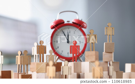 Wooden figurines with one red figure stand next to alarm clock 110618985