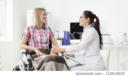 Smiling doctor communicates with patient in wheelchair 110619035