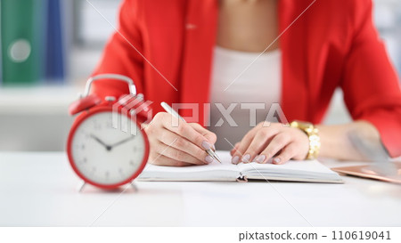 Businesswoman makes notes in documents there is an alarm clock next to it Businesswoman makes notes in documents there is an alarm clock next to it 110619041