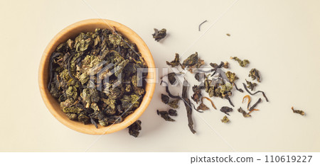 Dried tea leaves in wooden bowl on light beige background, top view Dried tea leaves in wooden bowl on light beige background, top view 110619227