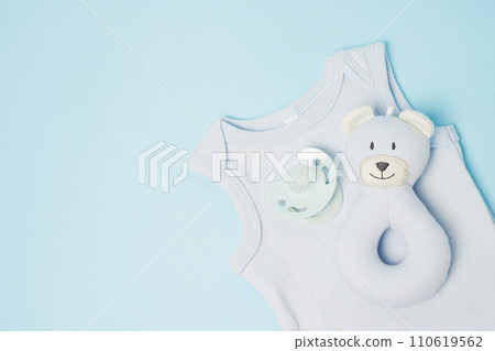 Clothes, toy and pacifier for newborn boy on blue table with copy space. Baby background - blue color Clothes, toy and pacifier for newborn boy on blue table with copy space. Baby background - blue color 110619562