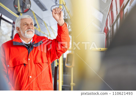 Front view of pensive grizzled male wearing red jacket standing looking at window inside public transport. Close up of mature man holding handle travelling by bus. Concept of city life. Front view of pensive grizzled male wearing red jacket standing looking at window inside public transport. Close up of mature man holding handle travelling by bus. Concept of city life. 110621493