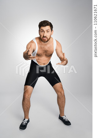 Angry wrestler in black and white singlet getting ready to attack, while looking at camera. Front view of male athlete grimacing, while staying in wrestling stance, isolated on white. Sport concept. 110621671