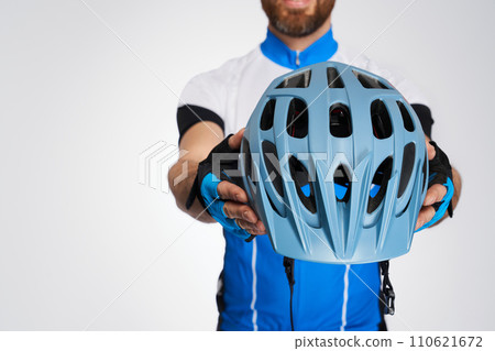 Unrecognizable bearded cyclist demonstrating modern helmet to camera. Close up view of protective helmet, showed by man in cycle kit, isolated on white studio background. Concept of sport and safety. Unrecognizable bearded cyclist demonstrating modern helmet to camera. Close up view of protective helmet, showed by man in cycle kit, isolated on white studio background. Concept of sport and safety. 110621672