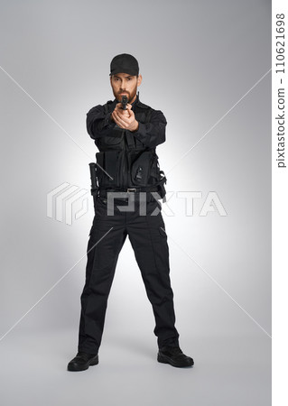 Caucasian cop holding automatic pistol gun, aiming to camera target. Front view of focused guy in police uniform shooting, while looking at camera, on gray background. Concept of body guard, work. 110621698