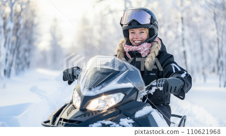 Happy young woman on a snowmobile outdoors on a sunny winter day. Beautiful girl riding outside on a cold winter day. Girl on a snow mobile. 110621968