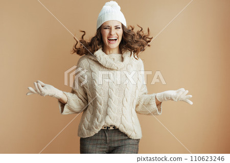 smiling trendy woman in beige sweater, mittens and hat jumping 110623246