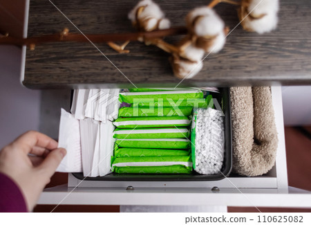 Sanitary napkin, tampon and cotton plant flower. Women hands pull out drawer containing hygiene products to help with menstruation. Cotton flower symbolizes absence of plastic. Made from eco materials 110625082