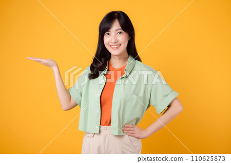 Vibrancy and joy portrait Asian young woman wears pastel green shirt on orange shirt and show happy smile while pointing hand gesture to free copy space. Perfect for adding lively touch to projects. 110625873