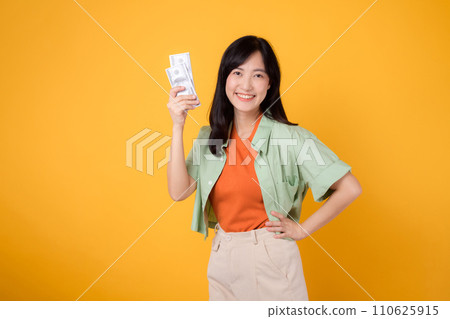 Asian woman 30s holding currency dollar while confidently placing hand on hip isolated on yellow background, embodies financial empowerment and style. financial stability and personal success concept. Asian woman 30s holding currency dollar while confidently placing hand on hip isolated on yellow background, embodies financial empowerment and style. financial stability and personal success concept. 110625915