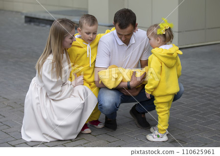 Mom and dad show the children a newborn baby. A baby has appeared in the family. Meeting your newborn brother or sister. Family with children at the maternity hospital. 110625961