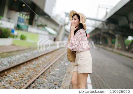 young asian woman traveler with weaving basket happy smiling looking to a camera beside train railway. Journey trip lifestyle, world travel explorer or Asia summer tourism concept. young asian woman traveler with weaving basket happy smiling looking to a camera beside train railway. Journey trip lifestyle, world travel explorer or Asia summer tourism concept. 110626060