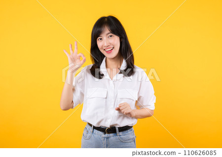 Young businesswoman hand sign okay gesture. Asian woman happy smile wearing white shirt and jean denim plants showing okay sign hand gesture isolated on yellow background. Young businesswoman hand sign okay gesture. Asian woman happy smile wearing white shirt and jean denim plants showing okay sign hand gesture isolated on yellow background. 110626085