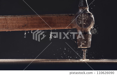 An old hammer hits a nail close-up on dark background. Dust rises from the impact. Carpentry concept. 110626090