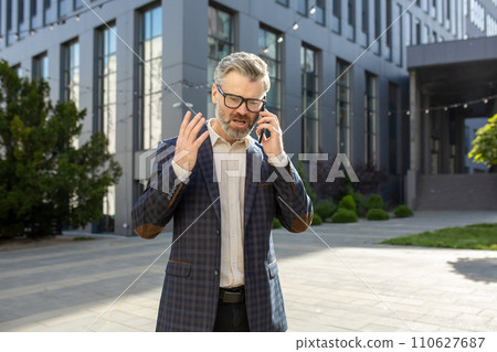 A senior executive in a checkered suit talks on his mobile phone, discussing important business while standing near an office building. A senior executive in a checkered suit talks on his mobile phone, discussing important business while standing near an office building. 110627687